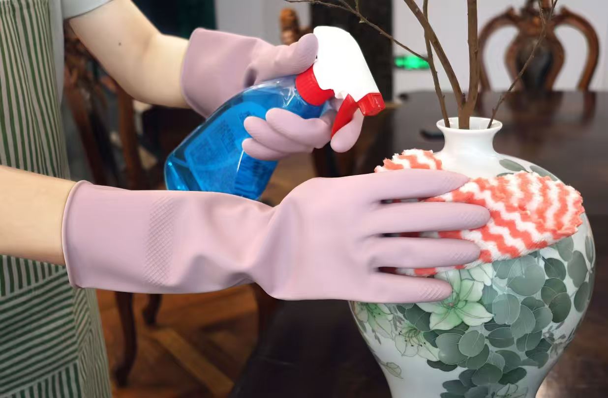 Lavender latex gloves cleaning a vase with a spray bottle